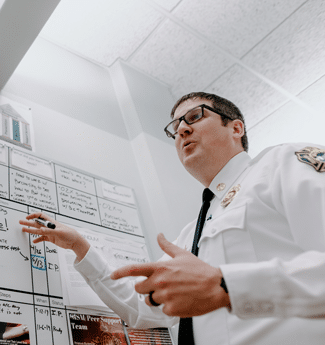 Male doctor of education graduate pointing to a whiteboard as he presents to his fire department team