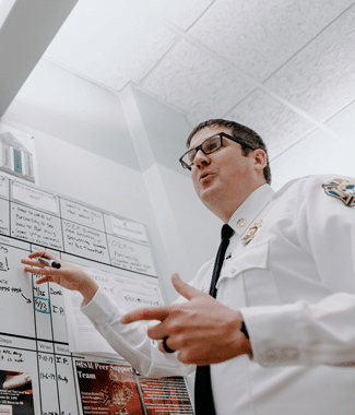 Male doctor of education graduate pointing to a whiteboard as he presents to his fire department team