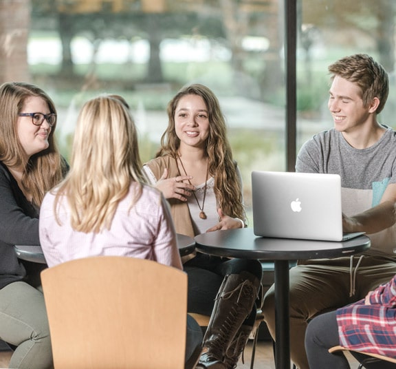 Male and female students meeting at a table with an open laptop in the Corum Student Union at Cornerstone University