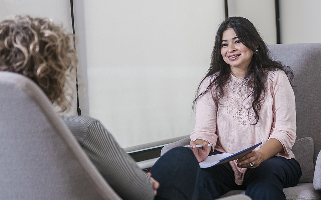 Female student holding a notepad and pen while meeting with a client in a counseling office