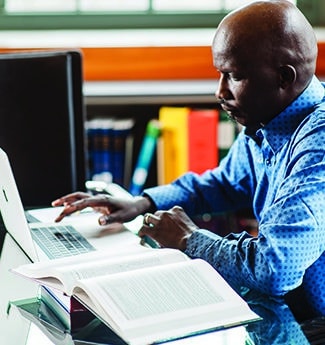 Male student working at a table with an open book and a laptop