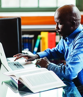 Male student working at a table with an open book and a laptop
