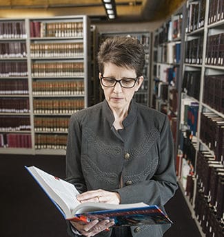 Female adult business student standing in library reading an open textbook
