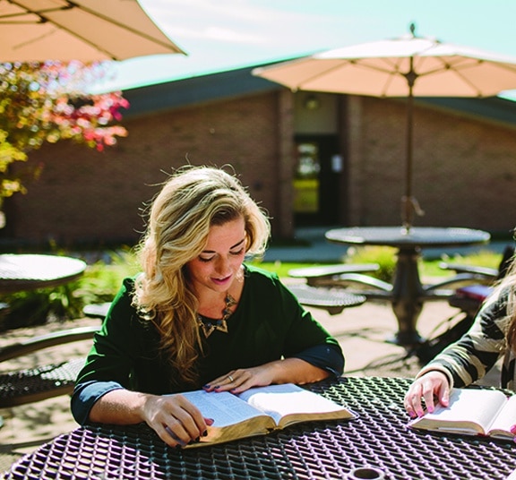 Female college student reading Bible at a picnic table