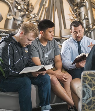 Male professor leading a bible study with male college students in lobby with metal sculpture