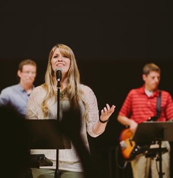Female at microphone with band leading singing in Christ Chapel at Cornerstone University