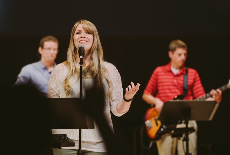 Female at microphone with band leading singing in Christ Chapel at Cornerstone University