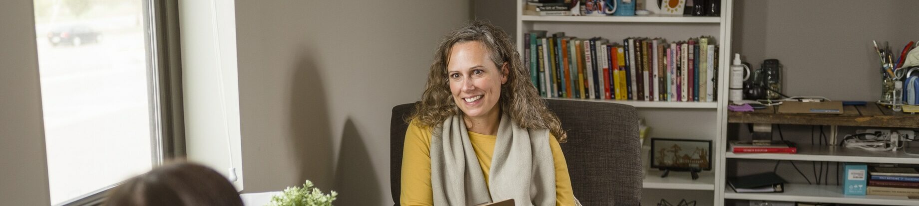 Adult female counselor holding a clipboard and pen while meeting with a client in a counseling office