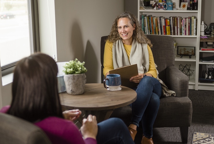 Adult female counselor holding a clipboard and pen while meeting with a client in a counseling office