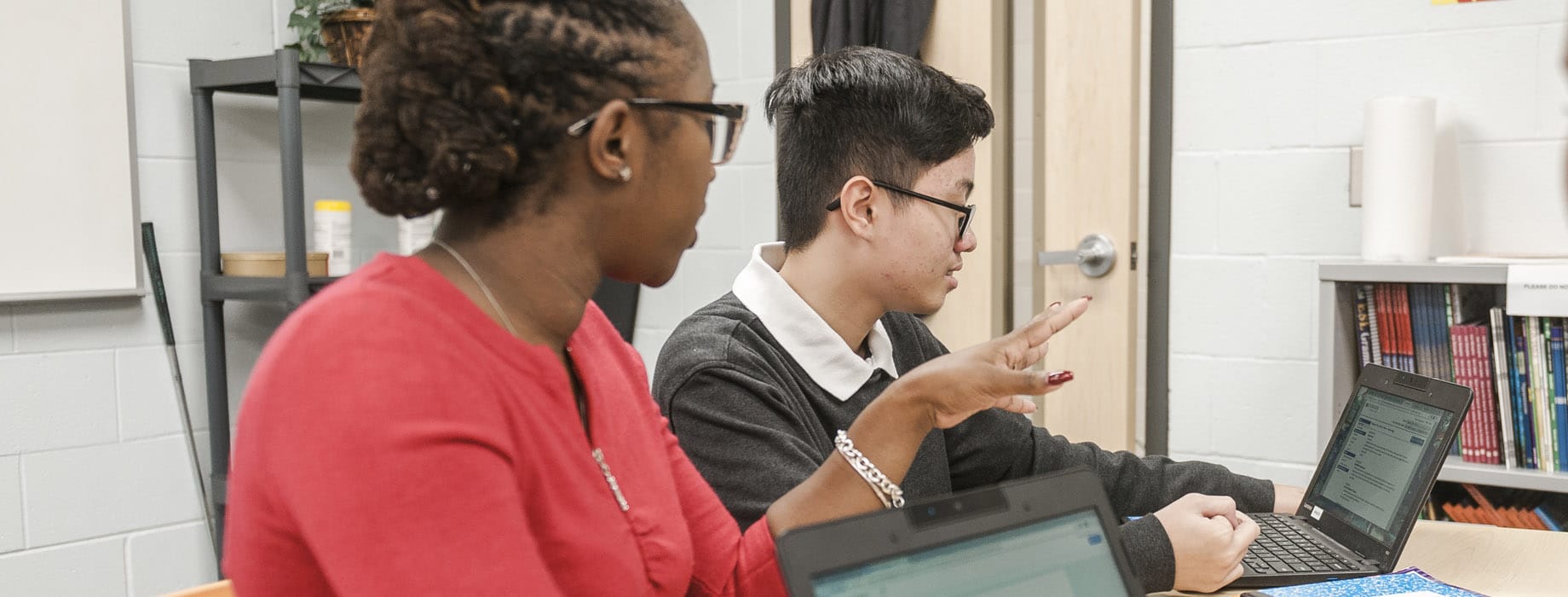 Female graduate student from Cornerstone University teaching at a table with one student with an open laptop