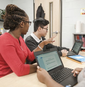 Female graduate student from Cornerstone University teaching at a table with one student with an open laptop