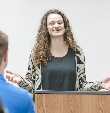 Female graduate student leading class discussion at white board while standing behind a podium