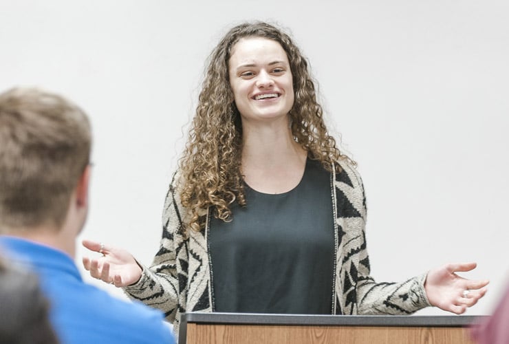 Female graduate student leading class discussion at white board while standing behind a podium