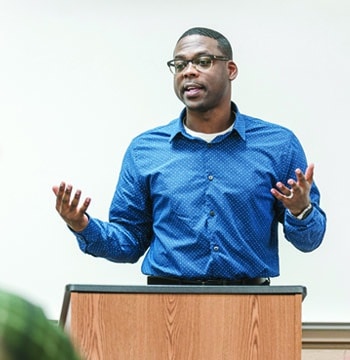 Male student speaking in front of classroom while standing behind a wooden podium