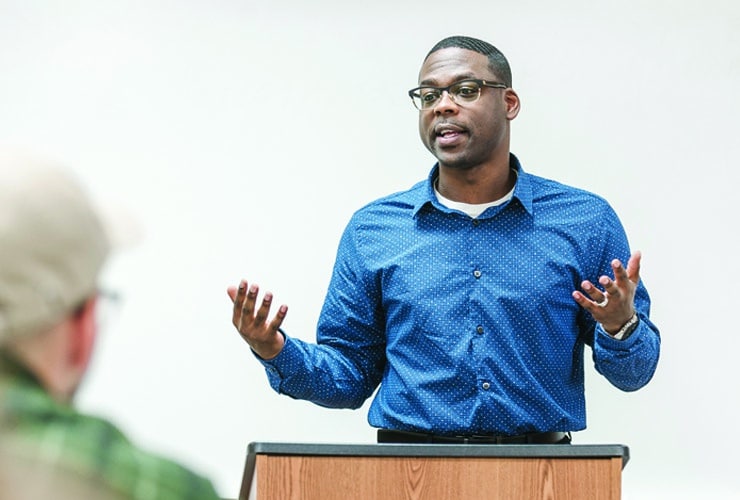 Male student speaking in front of classroom while standing behind a wooden podium