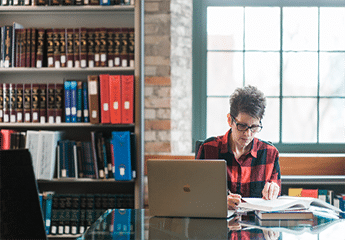 Female student at Cornerstone University working at a table with a laptop and open textbooks