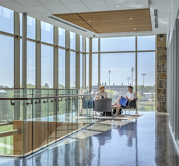 Two college students sitting in chairs by windows to study on the second floor of an academic building