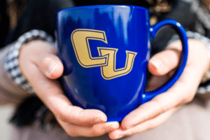 Hands holding a coffee mug with the letters CU