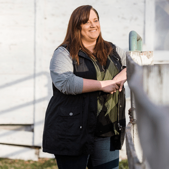 Female adult psychology student standing outside her home against a white fence