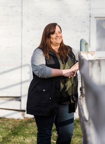 Female adult psychology student standing outside her home against a white fence