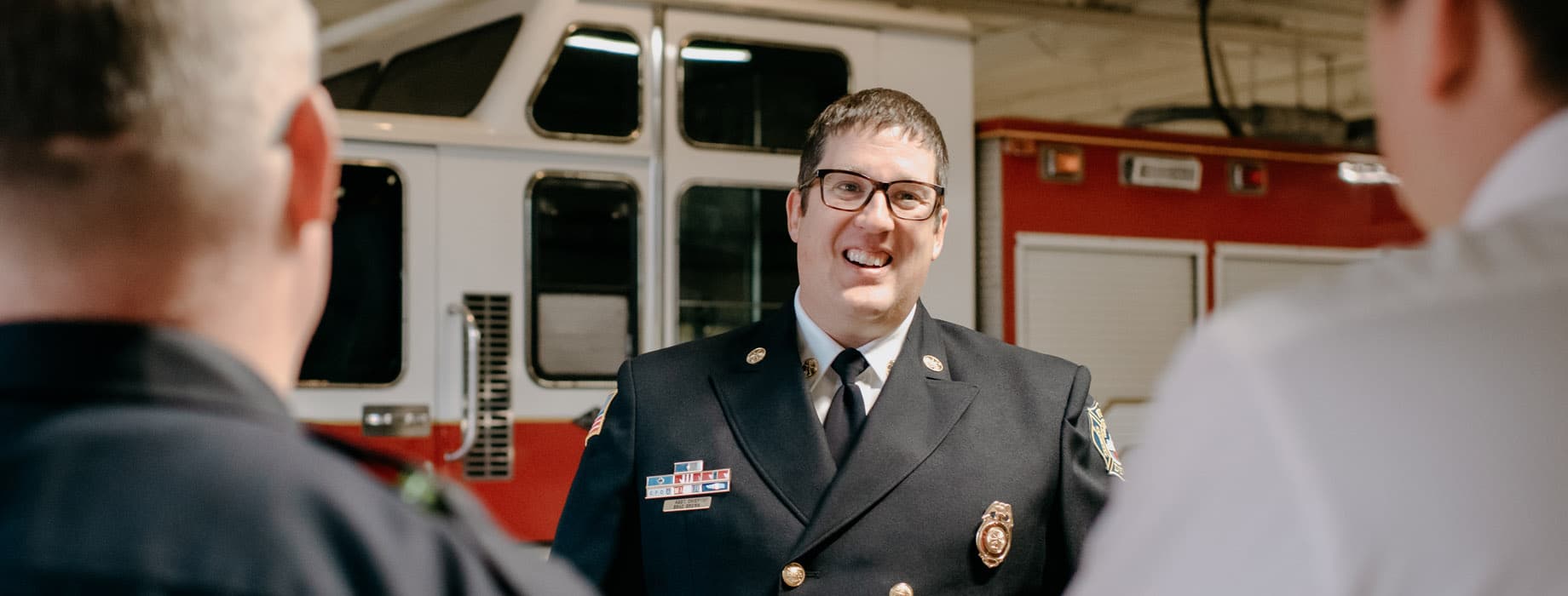 Male leader in uniform talking to three employees in fire department garage
