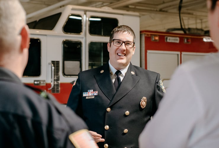 Male leader in uniform talking to three employees in fire department garage