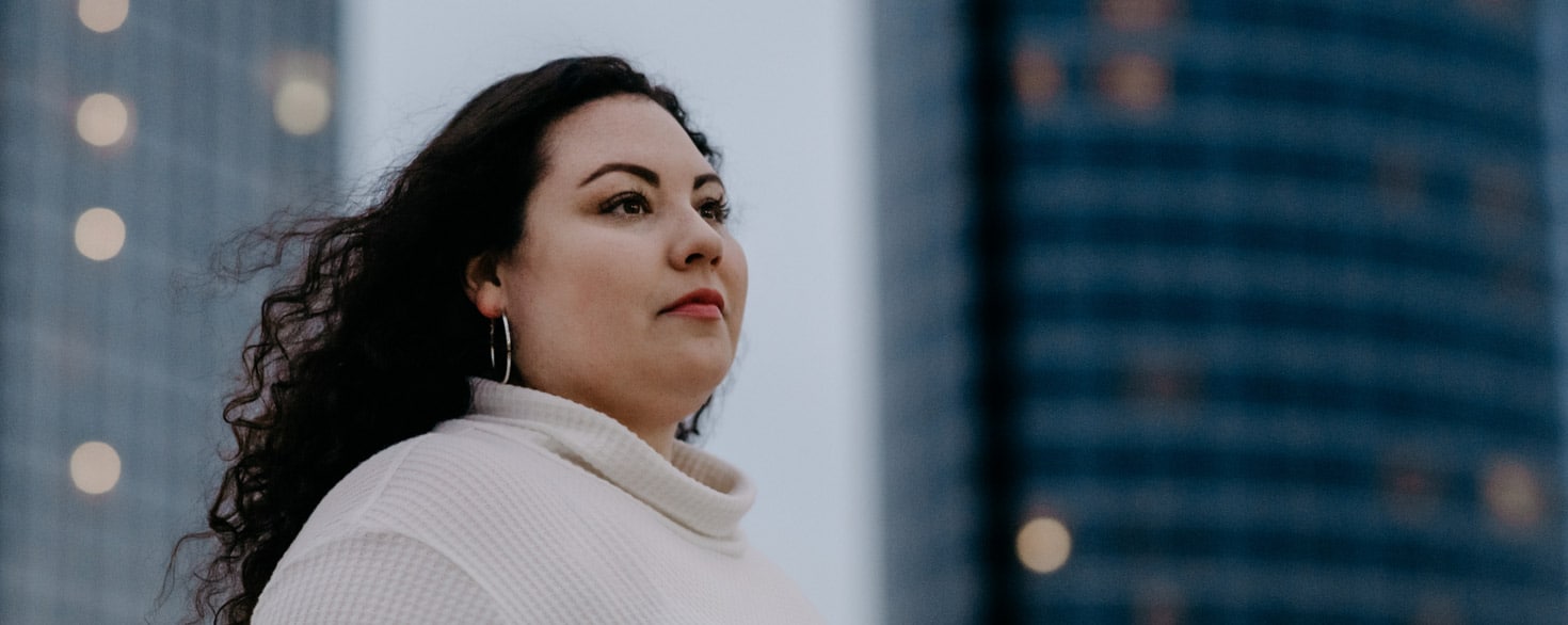 Adult female looking in the distance while standing in downtown Grand Rapids, Michigan, with buildings in the background