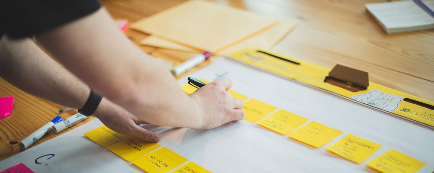 Person writing on sticky notes organized in a row on a desk