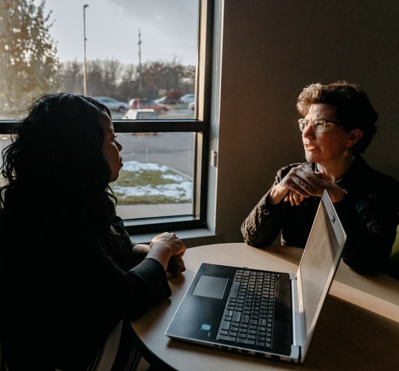 Adult female student with laptop meeting with female faculty member at a table at sunset