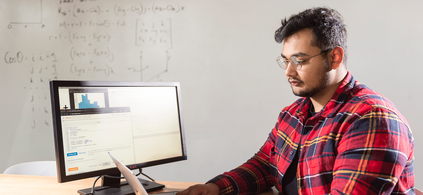 Male student typing on a laptop in a data engineering classroom