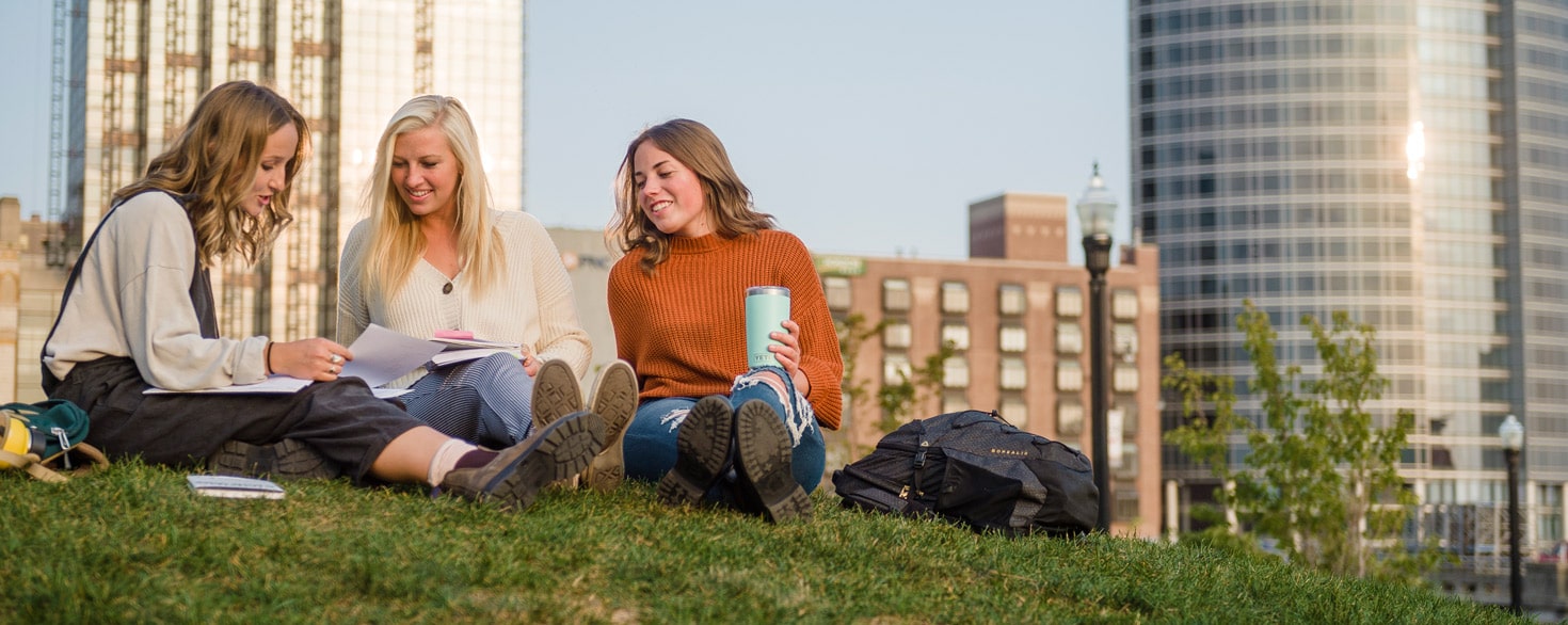 Three undergraduate students from Cornerstone University studying outside on grassy hill in Grand Rapids, Michigan