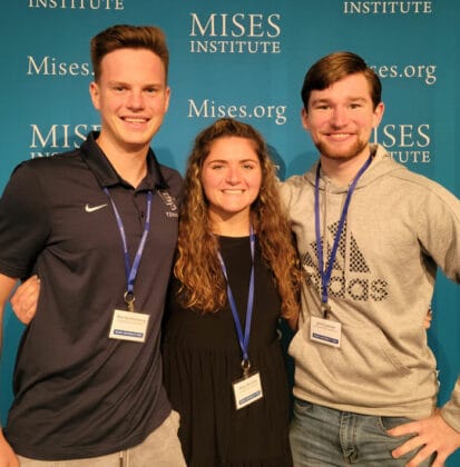 Two male and one female college student stand in front of banner that says Mises Institute