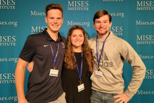 Two male and one female college student stand in front of banner that says Mises Institute