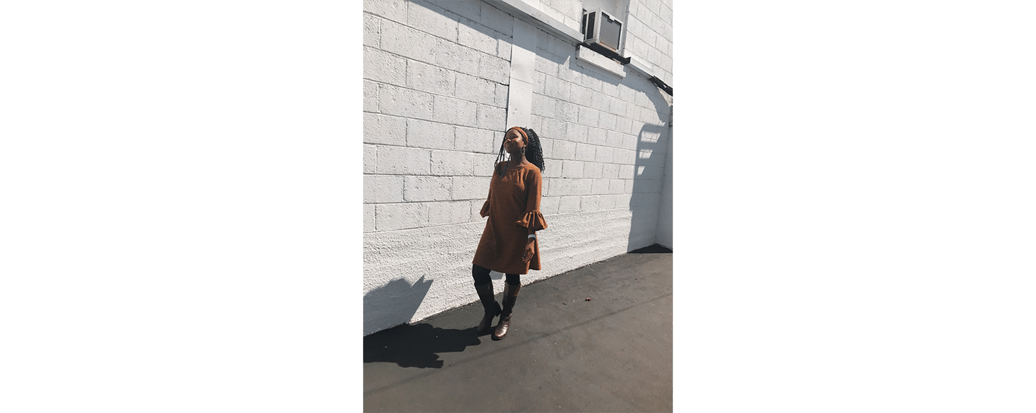 CU student Bianca Jones walking outside by a cinder block wall painted white