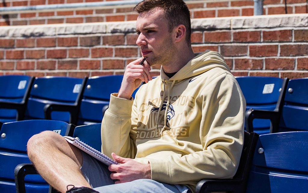 Male student sitting in bleachers while holding a notebook at Cornerstone University