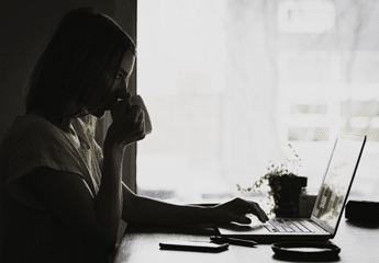 Girl drinking coffee while looking at a laptop set on a kitchen table