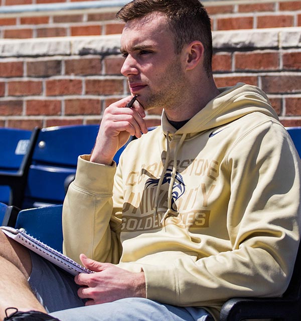 Male student sitting in bleachers while holding a notebook at Cornerstone University