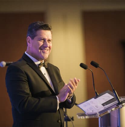 Gerson Moreno-Riaño stands behind a podium at Cornerstone University's Inaugural Gala in a tuxedo