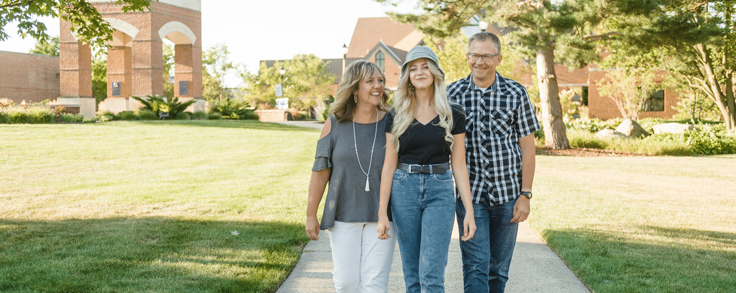 Female college student walking with mother and father on college campus sidewalk on a sunny day