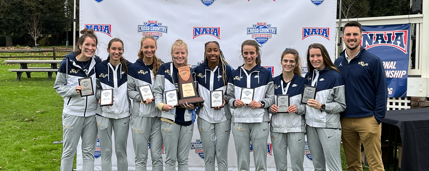 Cornerstone University women's cross country team and coach holding awards after a championship meet