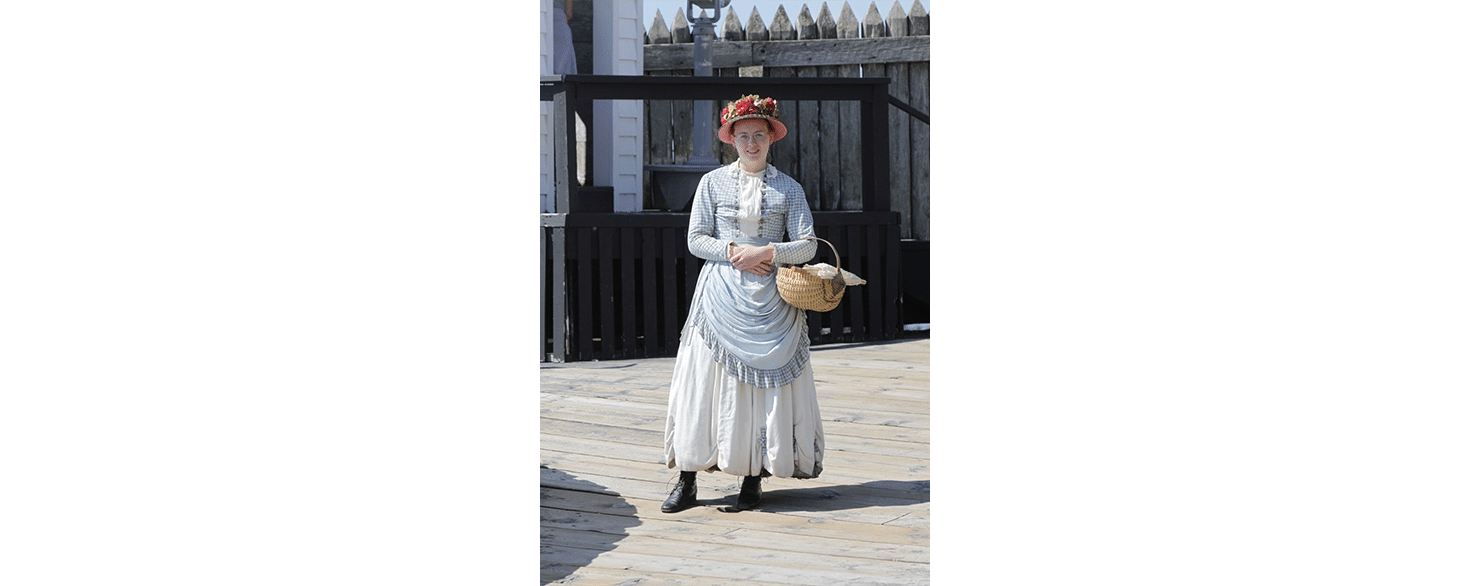 History student dressed in period costume for an internship assignment while wearing a hat and carrying a basket on her arm