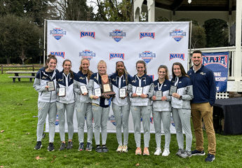 Cornerstone University women's cross country team and coach holding awards after a championship meet