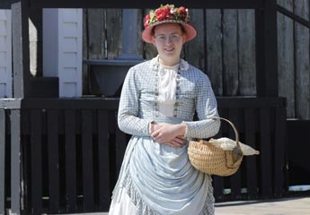 History student dressed in period costume for an internship assignment while wearing a hat and carrying a basket on her arm