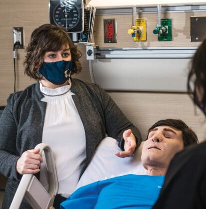 Female nursing instructor oversees one student training on a mannequin in simulated hospital setting