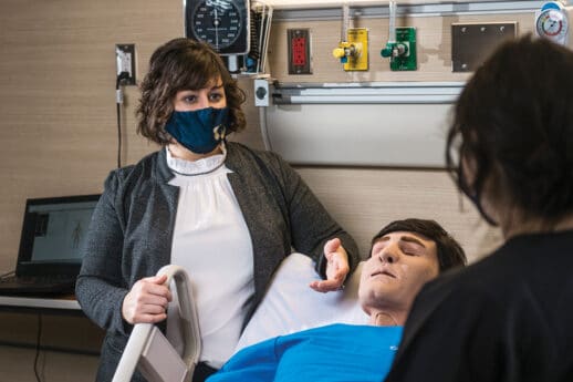 Female nursing instructor oversees one student training on a mannequin in simulated hospital setting