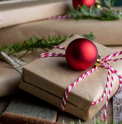 Christmas gifts wrapped in brown paper and tied with red and white striped twine with pine branches and round ornaments