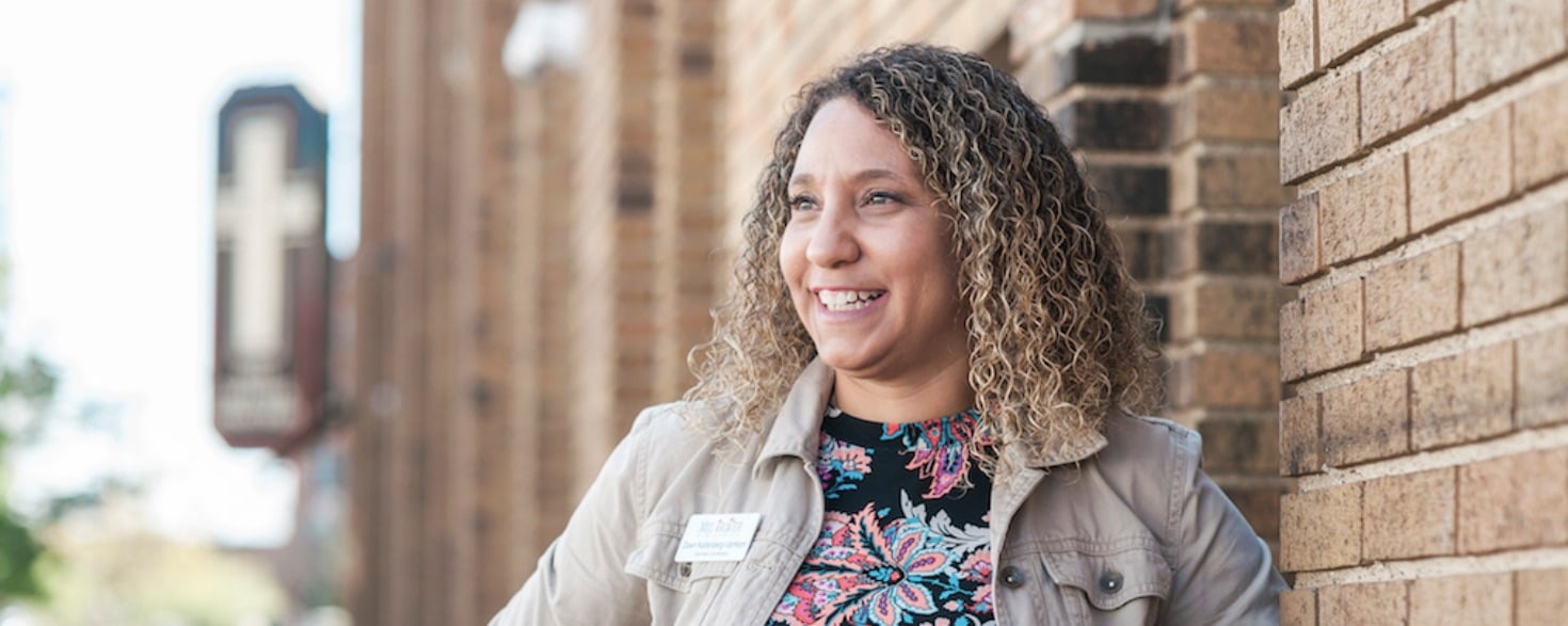Smiling female student leaning against a brick wall