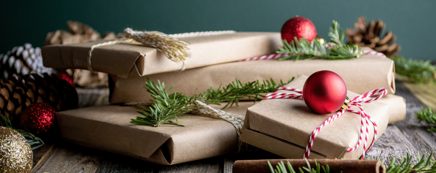 Christmas gifts wrapped in brown paper and tied with red and white striped twine with pine branches and round ornaments