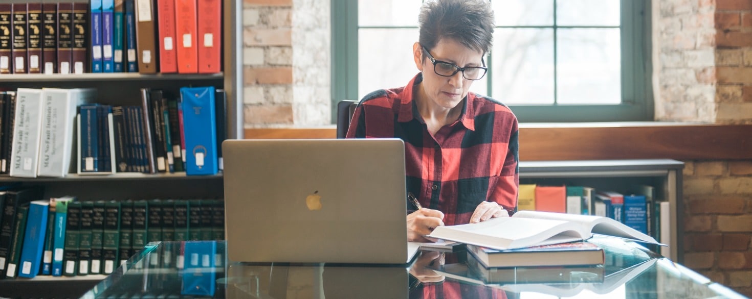 Female student at Cornerstone University working at a table with a laptop and open textbooks