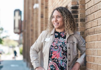 Smiling female student leaning against a brick wall